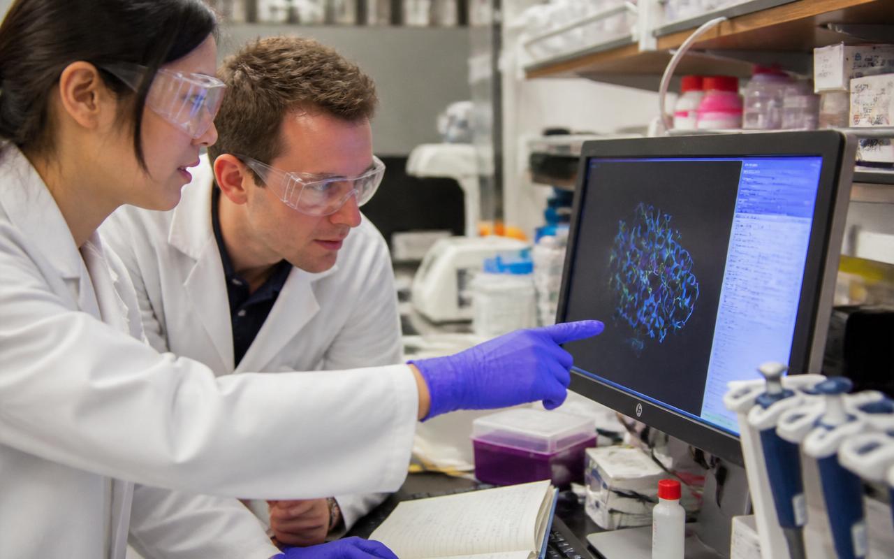 Two researchers in lab coats reviewing a molecular structure on a laboratory screen